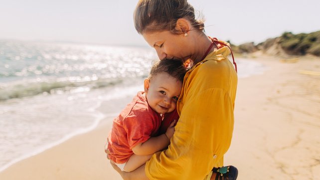 Woman holding and cuddling young child on beach