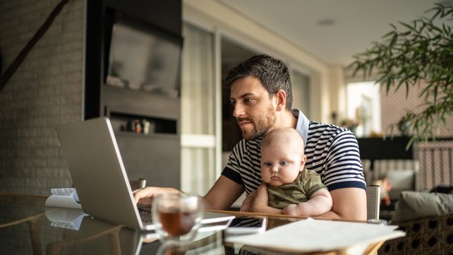 Man with baby on lap at kitchen table looking at laptop