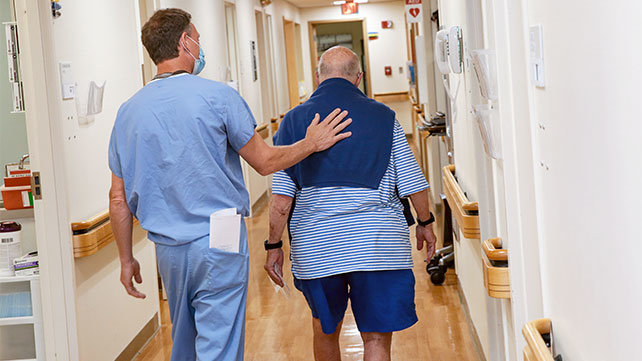 A clinician walks in the hospital hallway with a patient.