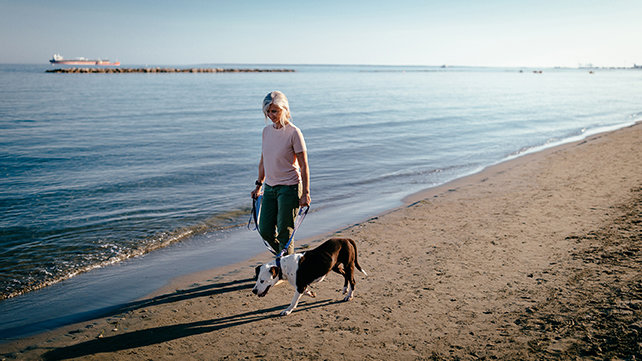 A woman walking her dog along a beach.